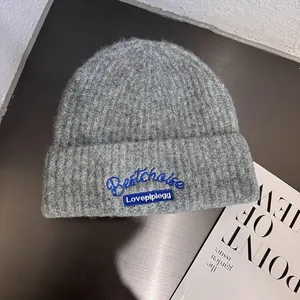 Close-up of gray ribbed knit beanie with blue letter embroidery on folded brim