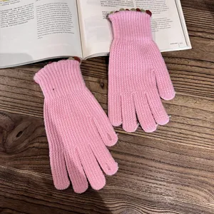 Pink knit gloves with colorful wavy cuff details on a cozy wooden tabletop background