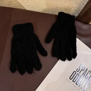 Close-up of black coral fleece gloves with elastic ribbed cuffs on a textured background