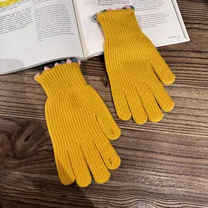 Detail of yellow knit gloves with colorful wavy cuffs on a wooden table with an open book