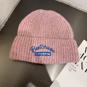 Detail of pink-purple knit beanie with blue embroidered Bestchoise logo on dark background