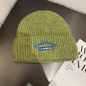 Detail view of grass green knitted beanie with blue letter embroidery and ribbed texture