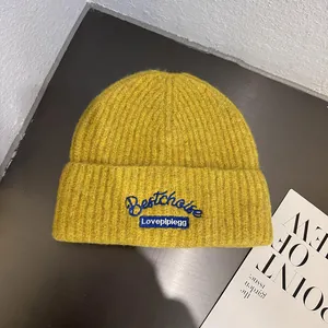 Detailed macro shot of mustard yellow ribbed knit beanie featuring an embroidered oval patch