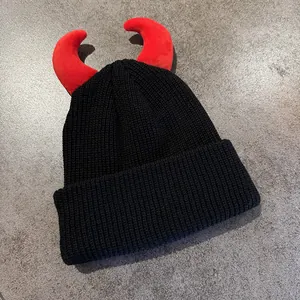 Dettaglio del cappello in maglia nera con corna da diavolo rosse su fondo grigio
