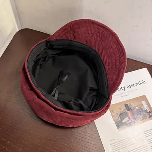 Detail of burgundy suede baker boy hat with adjustable inner ribbons on a wooden desk