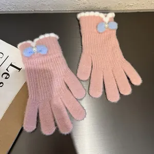 Dettaglio di guanti in maglia rosa con polsini smerlati bianchi e un fiocco in peluche blu