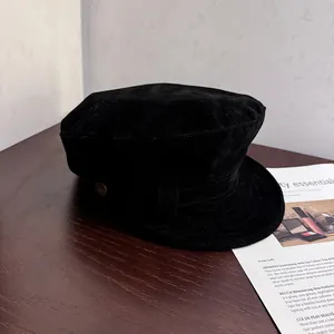 Detail of black suede newsboy cap with decorative metal button and structured vintage rim