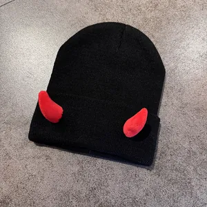 Dettaglio del berretto in maglia nera con corna da diavolo rosse e trama a costine