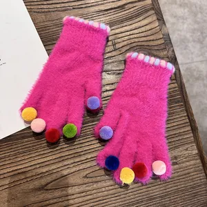 Detailansicht der plüschigen rosaroten Winterhandschuhe mit bunten Pompons auf dunklem Holz