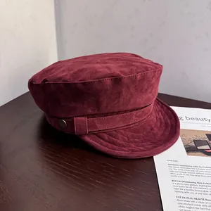 Detail of burgundy faux suede newsboy cap featuring vintage metal button and texture