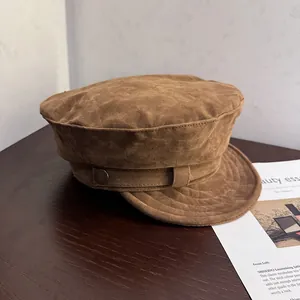Detail of a brown suede newsboy cap featuring a side leather strap and bronze button