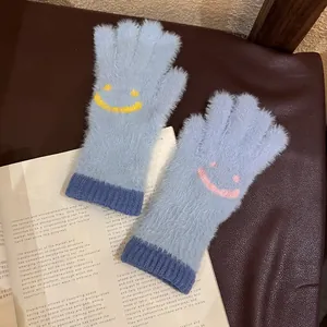 Détail de gants en peluche bleu clair avec visages souriants posés sur des pages de magazine