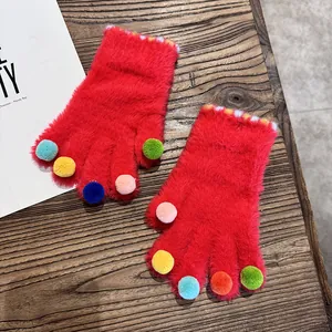 Nahaufnahme roter Plüschhandschuhe mit bunten Pompons und warmen Strickbündchen