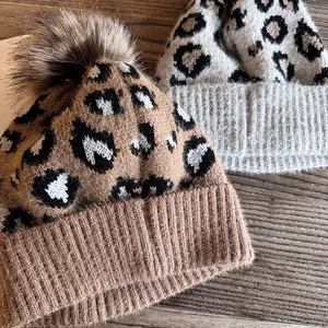 Outdoor-Strickmütze mit Leopardenmuster und flauschigem Pompon auf rustikalem Holz