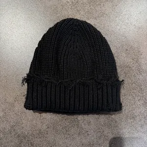 Close-up of black waffle knit beanie with distressed frayed edges and ribbed texture