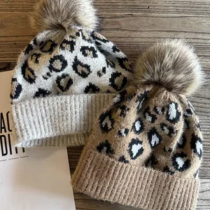Draufsicht auf Strickmützen mit Leopardenmuster und flauschigen Kunstfell-Bommeln auf Holz