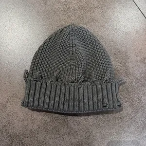 Close-up of dark grey distressed knit beanie showing ripped edges and ribbed texture