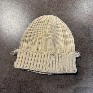 Detail view of beige knit beanie showing distressed rip textures and frayed edge style