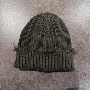 Detail of army green knit beanie showing waffle texture and distressed fringe edge