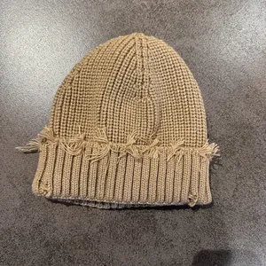 Detail of khaki ribbed knit beanie featuring vintage distressed ripped edge and frayed texture