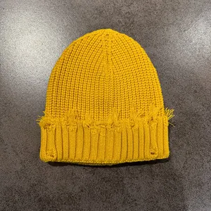 Detailed view of ginger yellow distressed knit beanie with frayed edges and torn design