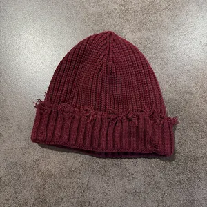 Detailed view of burgundy distressed knit beanie with vintage torn edges on stone background