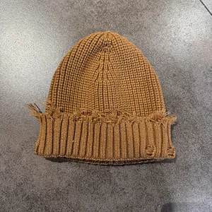 Detail of a brown knit beanie featuring retro distressed holes and frayed edge texture