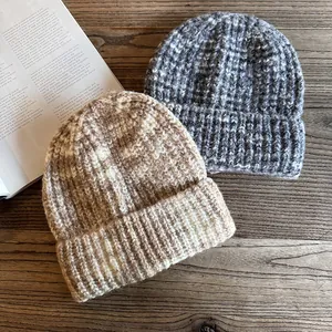 Chunky knit beanie hats in gradient beige and grey tones on a dark wood background