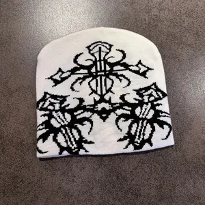 Close-up of white knit beanie featuring black gothic jacquard patterns and cross motifs