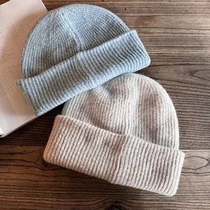 Berretti invernali in maglia a coste azzurro e beige su fondo legno per donna