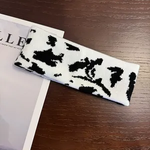 Knitted cow print headband for sports and casual wear placed on a wooden desk