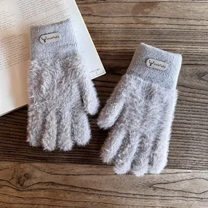 Detail von grauen Plüsch-Strickhandschuhen mit Rentier-Tag auf Holzuntergrund