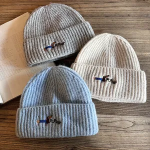 Detailed flat lay of three knitted beanies with puppy embroidery on a wooden table
