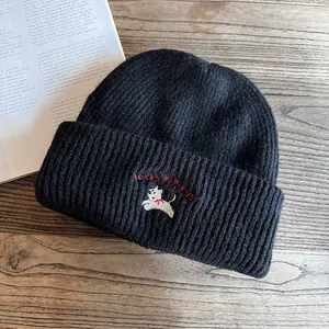 Dettaglio ravvicinato di un berretto in maglia nera con ricamo bianco di cucciolo lucky