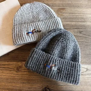 Knit beanie with dog embroidery in light and dark grey colors on a wooden surface