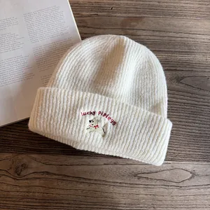 Dettaglio del ricamo a forma di cane sul caldo berretto in maglia bianco per donna