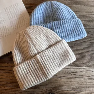 Detail of ribbed knit texture on light blue and beige beanies against a wooden background