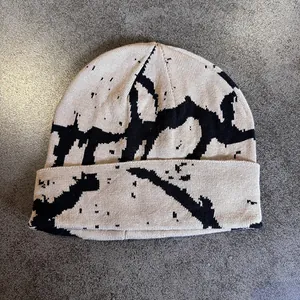Detailed close-up of beige knitted beanie featuring black abstract graffiti patterns