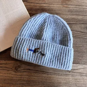 Detail of light blue ribbed knit beanie with embroidered dachshund on wood table