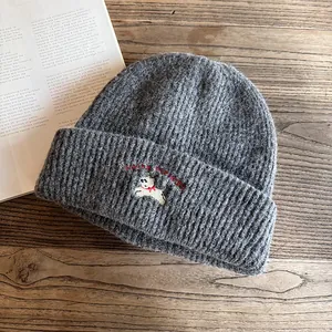 Dettaglio ravvicinato del berretto in maglia grigio scuro con ricamo di cane e lucky things