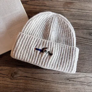 Detail of oatmeal knit beanie featuring a dachshund embroidery on a wooden table