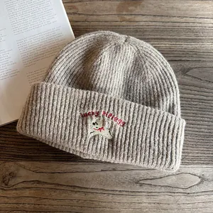 Dettaglio della trama del berretto in maglia beige con ricamo cucciolo e scritta Lucky