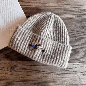 Detail of dachshund embroidery on khaki ribbed knit beanie over a wooden table