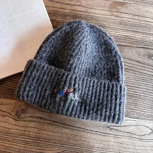 Detailed embroidery of a dachshund on a dark grey knit beanie with plush wool texture