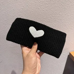 Close-up of a wide black knitted headband with a white heart embroidery and wool texture