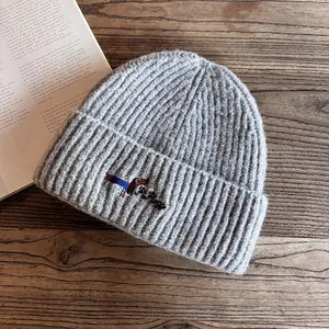 Close-up of light gray knit beanie with embroidered dachshund detail on a wooden table