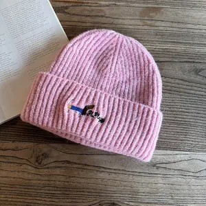 Detailed view of pink ribbed knit beanie with cute puppy embroidery on a wooden surface