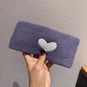 Close-up of a wide purple knitted headband featuring a white heart pattern and soft texture