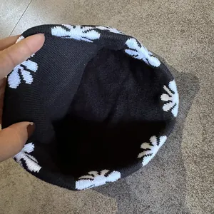 Detail of black knit beanie with white flower patterns showing elastic texture and fit