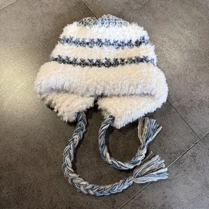 Detail of plush earflap hat with blue knit wave pattern and braided tassel strings